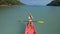 Pretty sportive blonde lady in stylish swimsuit sails on pink plastic canoe along azure ocean bay at exotic resort.