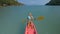 Pretty sportive blonde lady in stylish swimsuit sails on pink plastic canoe along azure ocean bay at exotic resort.