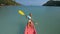 Pretty sportive blonde lady in stylish swimsuit sails on pink plastic canoe along azure ocean bay at exotic resort.