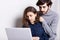 A pretty student helping her stylish boyfriend with his diploma paper. A hipster watching a presentation on laptop leaning at her