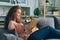 Pretty student reading book in apartment smiling and petting adorable dog