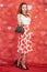 Pretty stylish pin up girl in white shirt and red polka dot vintage skirt standing on red hearts background