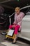 Pretty stylish young blonde woman in chic stylish pink fur coat in pants poses with paper bags in modern auto. Fashionable