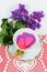 Pretty tea or coffee cup with silver trim filled with pink and purple paper hearts sitting on a white heart doily with a pink rose