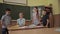 Pretty teacher in classroom sitting at the desk and asking children. education, elementary school, learning and people