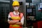 Pretty technician or worker woman with gray mask and yellow helmet stand with confident action in front of factory machine