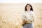 Pretty teen girl standing in a field among wheat. Girl holding a large bouquet of flowers in her hands