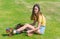 Pretty teenage girl in yellow top sits on grass putting retro style roller skates on