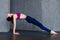 Pretty thin woman in sports bra and leggings doing yoga upward facing plank pose, purvottanasana, working out indoors