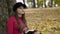 Pretty, thoughtful girl writing down in a notebook near a tree in autumn park