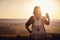 Pretty traveling woman standing on top of mountain at sunset and using mobile phone