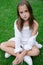 pretty tween girl in white clothes sitting on green grass outside in park on sunny summer day. charming ukrainian child