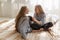 Pretty twin sisters in black jeans, striped shirts with long hair sit on sofa