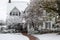 Pretty two story white clapboard house with shutters during a snow storm with sidewalk cleared and snow on the trees