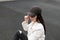 Pretty urban young woman in fashionable black baseball cap in a stylish white leather jacket relaxes and looks down outdoors.