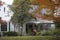 Pretty white house with overgrown yard and autumn leaves decorated with huge spider web and decorative flags for Halloween - frame