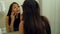 Pretty woman applying mascara eyelash in front of the mirror, while talking via smartphone in bathroom