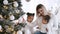 Pretty woman and daughters in white clothes sitting at Christmas tree at home