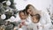 Pretty woman and daughters in white clothes sitting at Christmas tree at home