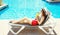 Pretty woman drinks juice from cup at summer on a deckchair over a blue water pool