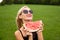A pretty woman on a field wearing photochromic glasses an appetizing slice of watermelon in a black hat from behind a beautiful