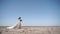 Pretty woman in gorgeous wedding dress walking at desert landscape, windy weather. Elegance bride with bouquet of fresh