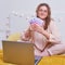 Pretty woman holds money in euros sitting on a home bed. Girl with a computer working remotely during isolation due to quarantine