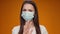 Pretty Woman in medical mask does disapproving gesture with her finger against yellow background