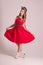 Pretty woman in red dress with hairdo stands in grey studio