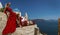 Pretty woman in red long evening dress is posing in Oia, Santorini Island. Female model in amazing long dress. Couture