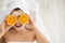 Pretty woman with rejuvenating facial mask holding sliced orange in spa salon