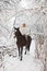 Pretty woman riding her horse through snow country road