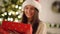 Pretty Woman in Santa Hat Astonished with the Surprise Inside of the Red Box. Cute Smiling Girl opening Christmas Gift