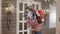 Pretty woman in santa`s hat hanging Christmas wreath on white door in house