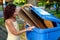 Pretty woman senior citizen seen lifting the lid of a blue recycling can overflowing with cardboard boxes