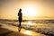 Pretty woman silhouette walks at seaside surf in golden sunset light. Girl having fun on ocean beach on summer