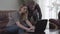 Pretty woman sitting on the leather sofa and bearded man standing near her working with laptop. Little girl comes with