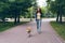 Pretty woman with smartphone walking shiba inu dog in park on summer day smiling