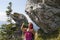 Pretty woman trekker drinking under big rock with signpost