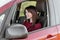 Pretty youDark-haired smiling girl in a burgundy sweatshirt driving a teracotta car