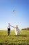 Pretty young adult wedding couple walking on field with kite