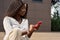 Pretty young African woman model using smartphone sitting outdoors.