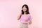 Pretty young asian woman showing success, victory hand gesture while receiving great news from smartphone on pink background.