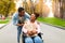 Pretty young black woman in wheelchair holding paper bag with products after shopping with her husband outdoors in fall