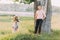 Pretty young blonde wearing lilac dress and wreath sitting in swing while her handsome boyfriend standing near tree