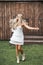 Pretty young boho-style blond woman, wearing feathers in the hair, white dress and cowboy boots, standing happy with