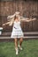 Pretty young boho-style blond woman, wearing feathers in the hair, white dress and cowboy boots, standing happy with