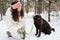 Pretty young brunette in winterwear looking at black retriever in park