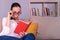 Pretty young brunette woman shocked reading a book sitting on the sofa at home.