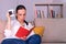 Pretty young brunette woman surprised reading a book sitting on the sofa at home and holding a cup of tea.